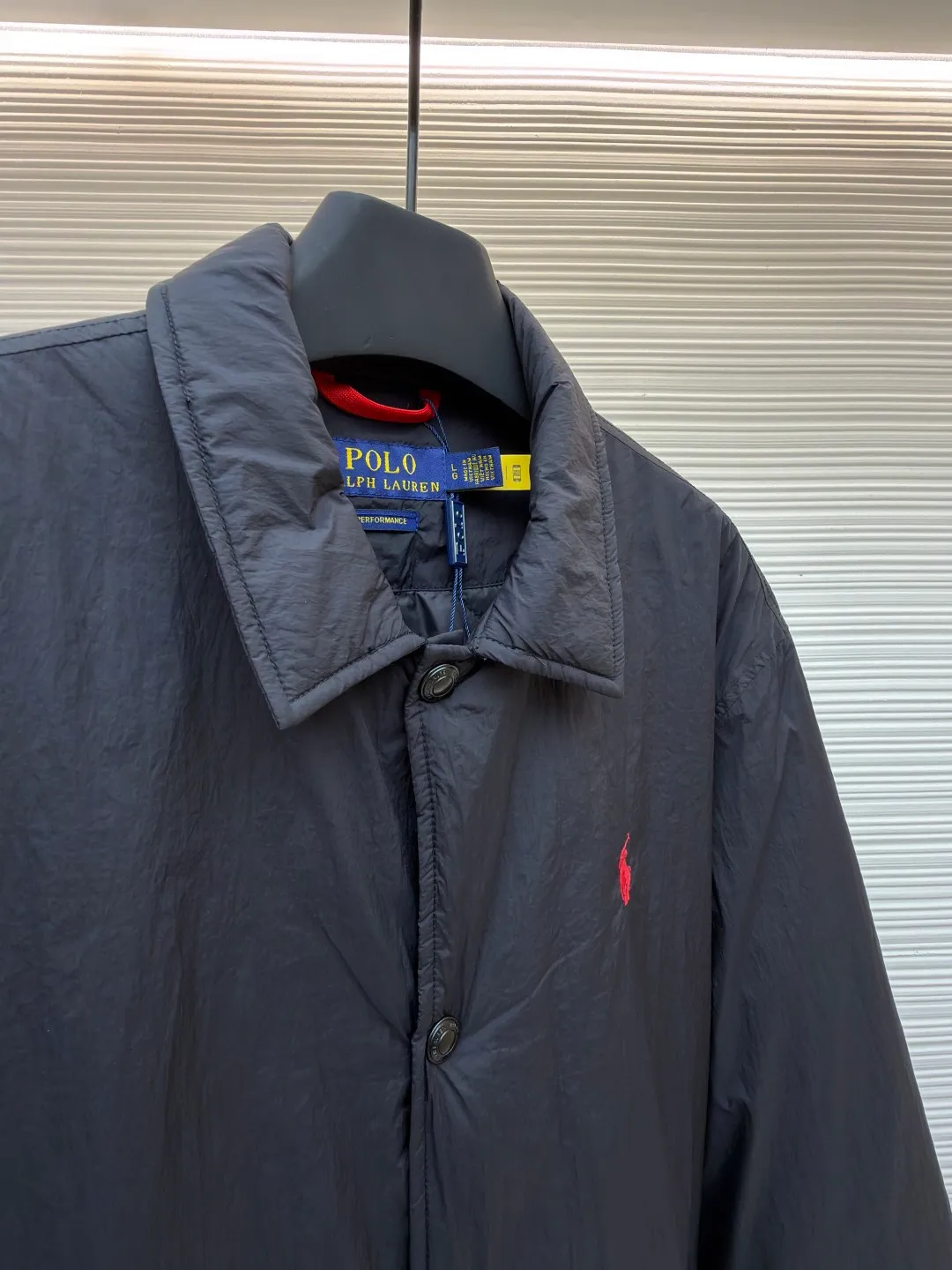 Ralph Lauren red label light cotton jacket (coach jacket) ●Original version: purchased and developed for 2699 ●Item number: 1681910-B90 ●Fabric: high-density nylon taffeta fabric ●Technology: embroidery production ●Color: black ●Version: fitted version ●Weight: about 340 grams ●Size: S-M-L-XL ●Description: The density of high-density nylon taffeta is about 210T-300T, with a smooth and slightly matte surface, excellent windproof and waterproof properties (with DWR water-repellent treatment), strong wrinkle resistance and easy care, in line with the positioning of American casual "durable and practical". Classic dark black, using vat dyeing process (dye penetrates into the fiber), the color fastness reaches ISO level 4 or above, preventing fading or color transfer after washing. The lightweight cotton-polyester blend lining (65% Polyester + 35% Cotton) reduces the friction between the fabric and inner clothing, improving the smoothness of wearing; the blended material combines breathability and durability to avoid the stuffy feeling of pure nylon lining. The classic Coach Jacket has a loose fit with slightly dropped shoulder lines (shoulder width is 1-2cm wider than the standard fit). The length reaches the hips and the sleeves are slightly tapered straight sleeves, taking into account both freedom of movement and casual style. Polo horse logo on the left chest: flat satin stitch embroidery (satin embroidery), embroidery thread: 100% polyester high color fastness embroidery thread (the color number is consistent with the brand's standard red color card), stitch density 12-15 stitches/cm, the outline of the horse logo is clear, and the details of the rider and horse are burr-free. Embroidery positioning: precise positioning through the template (12cm from the neckline and 8cm from the placket) to ensure left and right symmetry and centering. Topstitching technology: The seams of the body are made of double-needle flat seams (needle pitch 3cm/10 needles), the stitches are smooth and straight, the stitching color is dark black (the same color as the fabric), and the stitch width is 0.5cm, which enhances firmness while forming simple decorative lines. The splicing of the front placket and the body: the placket is made of double-layer folding + flat seam splicing, with a thickness of about 0.3cm to ensure that the buttons are not easily deformed when fixed; the edges of the placket are cut with a hot knife to avoid burrs. The sleeves are spliced ​​to the body: the armholes are spliced ​​with round-head keyhole machine seams + flat seams. After splicing, the armholes have a natural curvature and no sense of tightness during movement; the height of the sleeves is about 8-10cm, which is in line with the loose characteristics of casual jackets. Main button: black urea resin button, matte surface treatment, buttonholes are hand-made keyholes (6 strands of cotton thread, keyhole density 8 stitches/mm), and the edges of the eyelets are smooth and without burrs. Collar buttons: The first button on the collar is a hidden button (diameter 12mm), which prevents the collar from opening and improves the neatness of wearing.